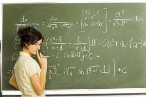 Teenage girl standing in classroom. Doing exercise on blackboard. Side view